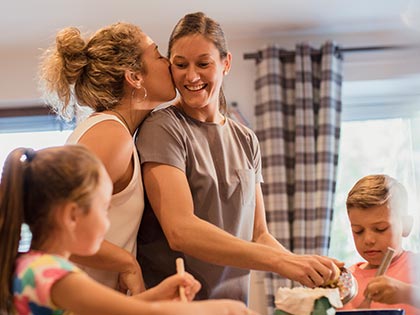 Two moms preparing a meal in a kitchen with their two kids